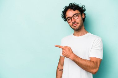Beyaz arka planda izole edilmiş genç beyaz bir adam gülümsüyor ve boş alanda bir şeyler gösteriyor..