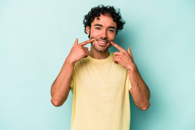 Beyaz arka planda izole edilmiş genç beyaz adam gülümsüyor, parmaklarını ağıza doğrultuyor..