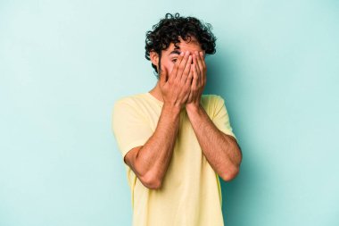 Beyaz arka planda izole edilmiş genç beyaz bir adam kameraya parmaklarıyla göz kırpıyor, yüzünü kapatmaktan utanıyor..