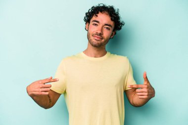 Beyaz arka planda yaşayan beyaz tenli genç bir adam gömlek fotokopi alanını gösteriyor, gururlu ve kendinden emin.