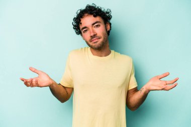 Beyaz arka planda izole edilmiş genç beyaz bir adam sorgulama sırasında omuz silkiyor ve şüphe duyuyor..