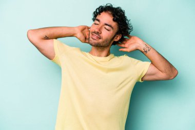 Beyaz arka planda izole olmuş genç beyaz bir adam kendini güvende hissediyor, elleri başının arkasında..