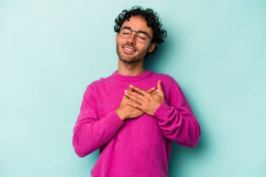 Beyaz arka planda soyutlanmış beyaz tenli genç bir adam gülüyor, elini yüreğine koyuyor, mutluluk kavramını koruyor..