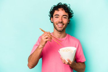 Mavi arka planda izole edilmiş erişte yiyen genç beyaz bir adam.