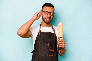 Genç İspanyol ayakkabıcı, mavi arka planda izole edilmiş kulakları elleriyle kapatıyor..