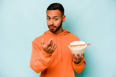 Mavi arka planda izole edilmiş erişte yiyen genç İspanyol kadın sanki seni davet ediyormuş gibi seni işaret ediyor..