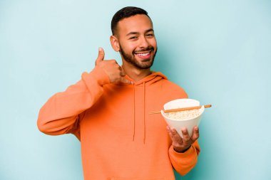 Mavi arka planda izole edilmiş erişte yiyen genç İspanyol kadın parmaklarıyla bir cep telefonu hareketi gösteriyor..