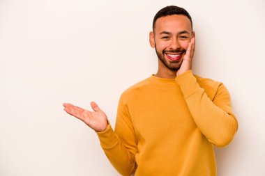 Beyaz arka planda izole edilmiş genç İspanyol bir adam avuç içinde fotokopi alanı tutuyor, el üstünde tutuyor. Şaşırmış ve mutlu..