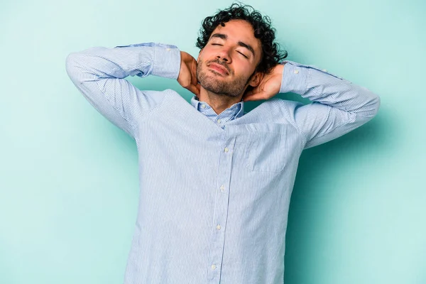 Beyaz arka planda izole olmuş genç beyaz bir adam kendini güvende hissediyor, elleri başının arkasında..