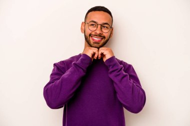 Beyaz arka planda izole edilmiş genç İspanyol adam ellerini çenesinin altında tutuyor ve mutlu bir şekilde yan tarafa bakıyor..