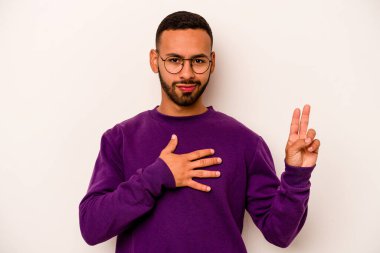 Genç İspanyol bir adam beyaz arka planda izole edilmiş yemin ediyor, elini göğsüne koyuyor..