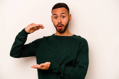 Beyaz arka planda izole edilmiş genç İspanyol adam iki eliyle bir şey tutuyor, ürün sunumu..