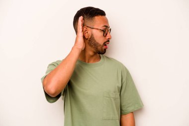 Latin kökenli genç bir adam beyaz arka planda bir dedikoduyu dinlemeye çalışıyor..