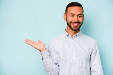 Mavi arka planda izole edilmiş genç İspanyol bir adam avucunun içinde bir fotokopi alanı ve belinde bir el daha gösteriyor..