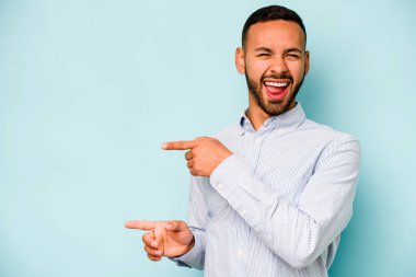 Mavi arka planda izole edilmiş genç İspanyol adam işaret parmaklarıyla fotokopi alanını işaret ederek heyecan ve arzuyu ifade ediyor..