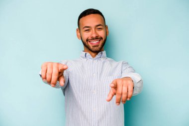 Mavi arka planda izole edilmiş genç İspanyol adam. Önü gösteren neşeli gülücükler..