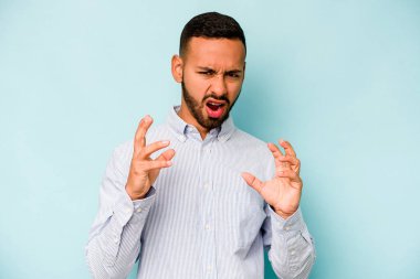 Mavi arka planda izole edilmiş genç İspanyol adam gergin elleriyle çığlık atıyor..
