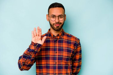 Genç İspanyol adam mavi arka planda izole edilmiş gülümsüyor beş numarayı parmaklarıyla gösteriyor..