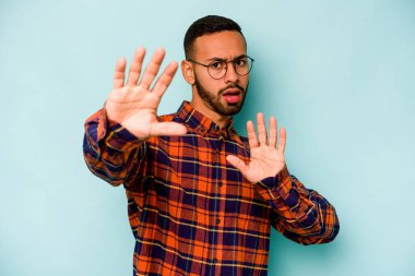 Genç İspanyol bir adam mavi arka planda izole edilmiş. Yakın bir tehlike nedeniyle şok oluyor.