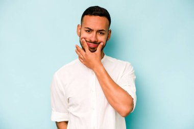 Latin kökenli genç bir adam mavi arka planda iki seçenek arasında kuşkulanıyor..