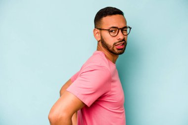 Genç İspanyol bir adam mavi arka planda izole edilmiş sırt ağrısı çekiyor..