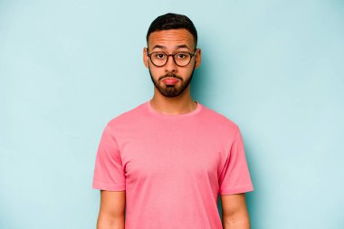 Genç İspanyol adam mavi arka planda izole edilmiş üzgün, ciddi yüz, mutsuz ve hoşnutsuz hissediyor.