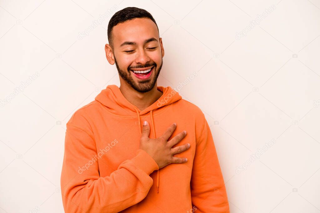 Young hispanic man isolated on white background laughs out loudly keeping hand on chest.