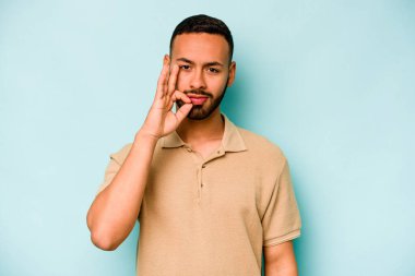 Genç İspanyol adam mavi arka planda izole edilmiş, parmakları dudaklarında bir sır saklıyor..