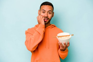 Mavi arka planda izole edilmiş erişte yiyen genç İspanyol kadın tırnaklarını yiyor, gergin ve çok endişeli..