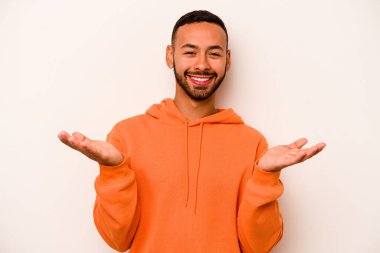 Beyaz arka planda izole edilmiş genç İspanyol adam kollarıyla ölçeği yapıyor, mutlu ve kendinden emin hissediyor..