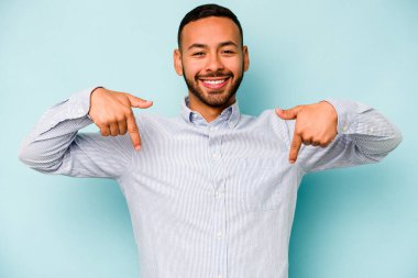 Genç İspanyol bir adam mavi arka planda izole edilmiş. Parmakları aşağıda, olumlu hisler içinde..