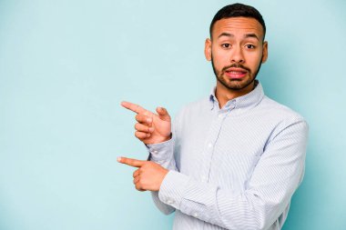 Mavi arka planda izole edilmiş genç İspanyol adam işaret parmağıyla fotokopi alanını işaret ederek şok oldu..
