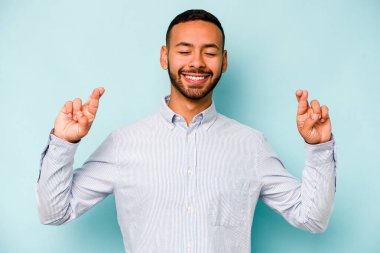 Genç İspanyol adam mavi arka planda izole edilmiş şans dilemek için şans diliyor.