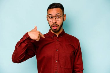 Mavi arka planda izole edilmiş genç bir İspanyol gömlek fotokopisini elle işaret ediyor, gururlu ve kendinden emin.