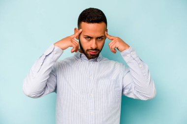 Mavi arka planda izole edilmiş genç İspanyol bir adam bir göreve odaklanmış, işaret parmaklarını işaret ediyor..