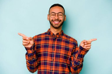 Mavi arka planda izole edilmiş genç İspanyol adam farklı kopya alanlarını gösteriyor, birini seçiyor, parmaklarıyla gösteriyor..