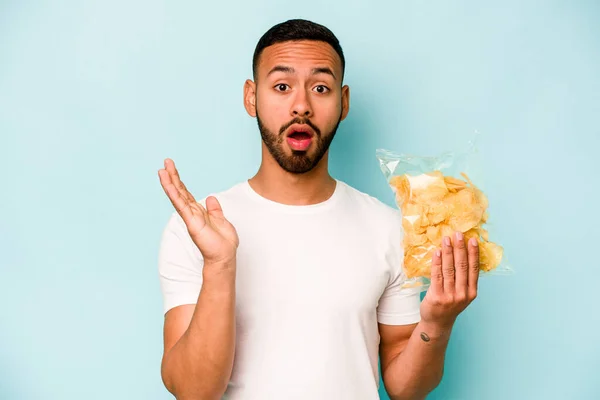Young Hispanic Man Holding Bag Chips Isolated Blue Background Surprised — Stock fotografie
