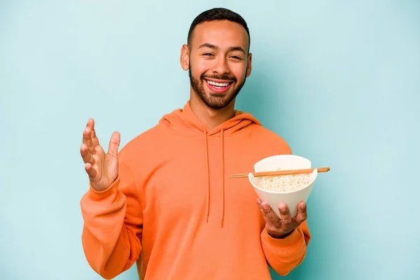 stock image Young hispanic woman eating noodles isolated on blue background receiving a pleasant surprise, excited and raising hands.