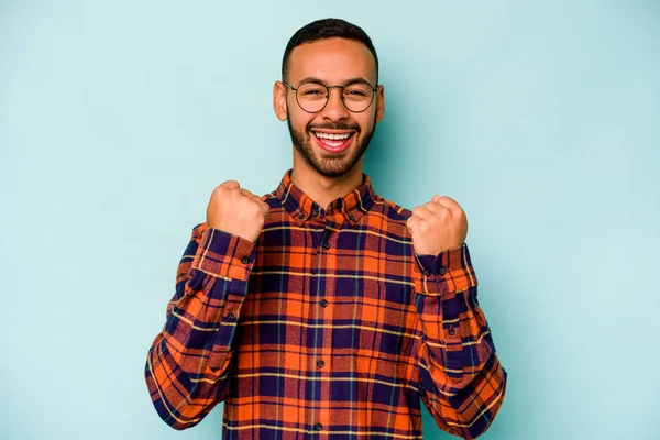 Genç İspanyol adam mavi arka planda izole edilmiş kaygısız ve heyecanlı tezahüratlar yapıyor. Zafer konsepti.