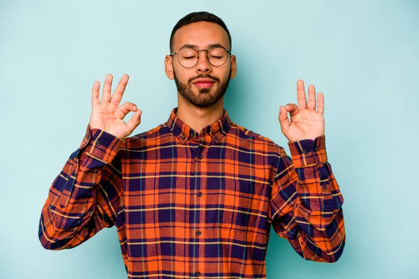 Mavi arka planda izole olmuş genç İspanyol adam sıkı çalışma gününden sonra rahatlıyor, yoga yapıyor..