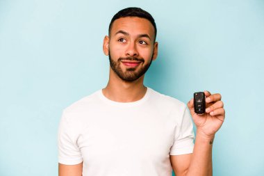 Young hispanic man holding car keys isolated on blue background dreaming of achieving goals and purposes