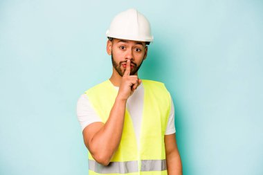 Genç bir işçi mavi arka planda izole edilmiş bir şekilde ya sır saklıyor ya da sessizlik istiyor..
