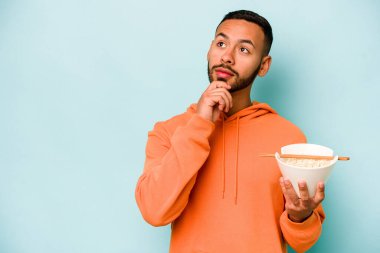 Mavi arka planda izole edilmiş erişte yiyen genç İspanyol kadın şüpheli ve şüpheci bir ifadeyle yana bakıyor..