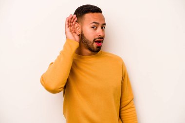 Latin kökenli genç bir adam beyaz arka planda bir dedikoduyu dinlemeye çalışıyor..