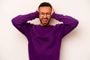 Latin kökenli genç adam beyaz arka planda izole edilmiş. Kulakları kulaklarıyla kapatıyor. Çok fazla ses duymamaya çalışıyor..