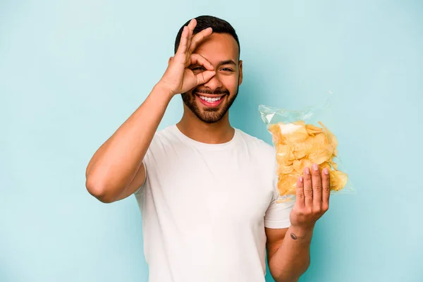 Young Hispanic Man Holding Bag Chips Isolated Blue Background Excited — Stock fotografie