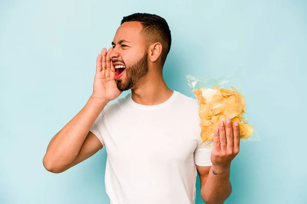Mladý Hispánec Drží Pytel Chipsů Izolovaných Modrém Pozadí Křičí Drží — Stock fotografie