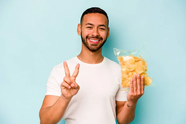 Young Hispanic Man Holding Bag Chips Isolated Blue Background Showing — Stock fotografie