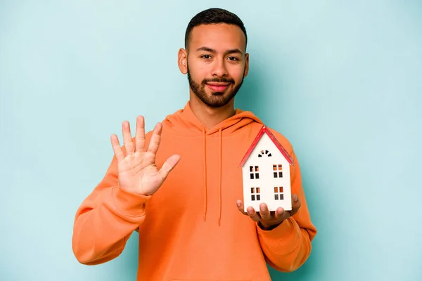 Young Hispanic Man Holding Toy House Isolated Blue Background Smiling — Zdjęcie stockowe