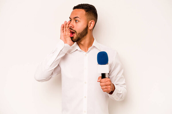 Young hispanic TV presenter isolated on blue background shouting and holding palm near opened mouth.